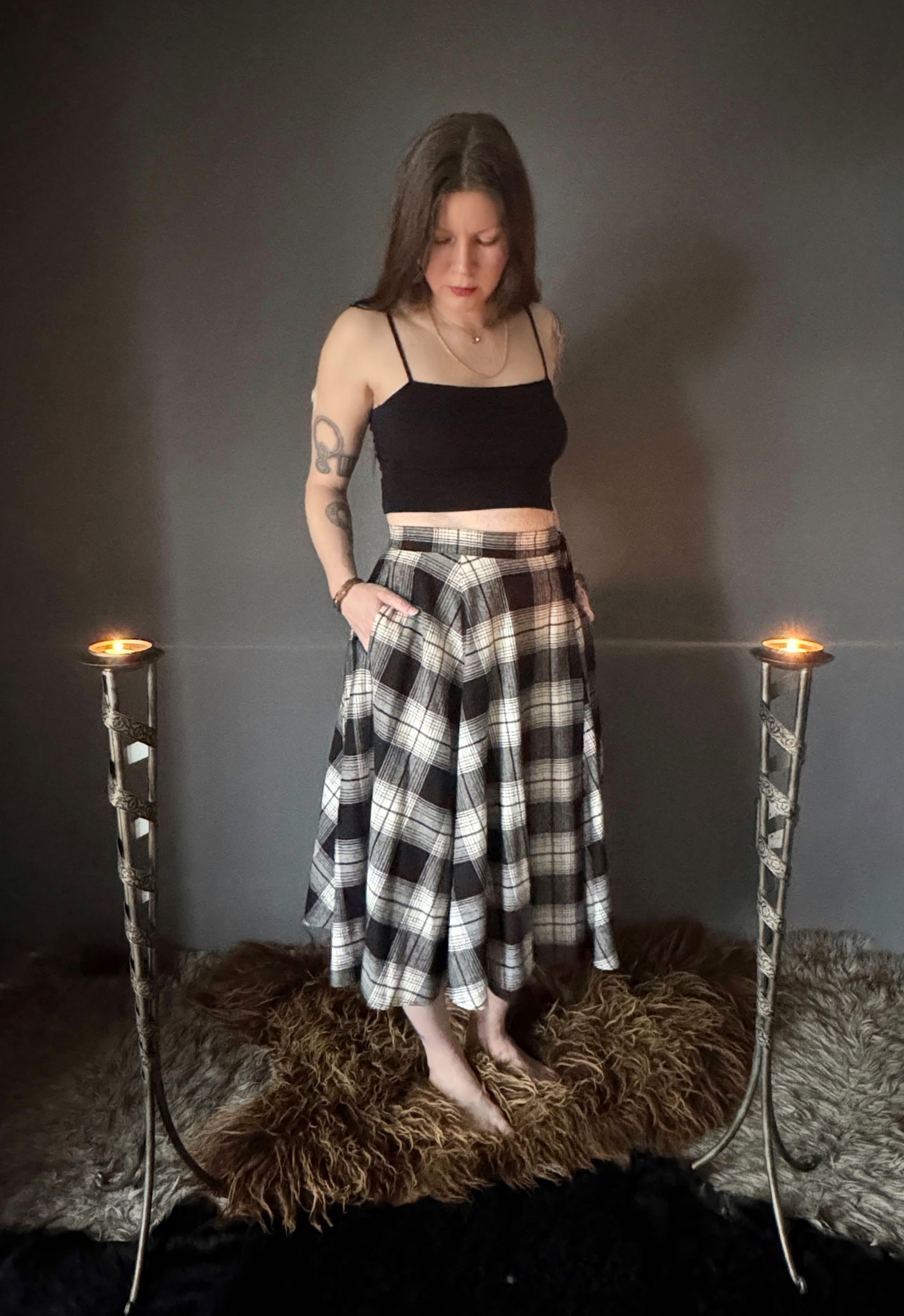 A photo of a black and white plaid wrap skirt.The photo is a from angled view featuring the mid calf length, side pockets and long ties. An adjustable cotton tartan wrap skirt, size inclusive and made in Canada.