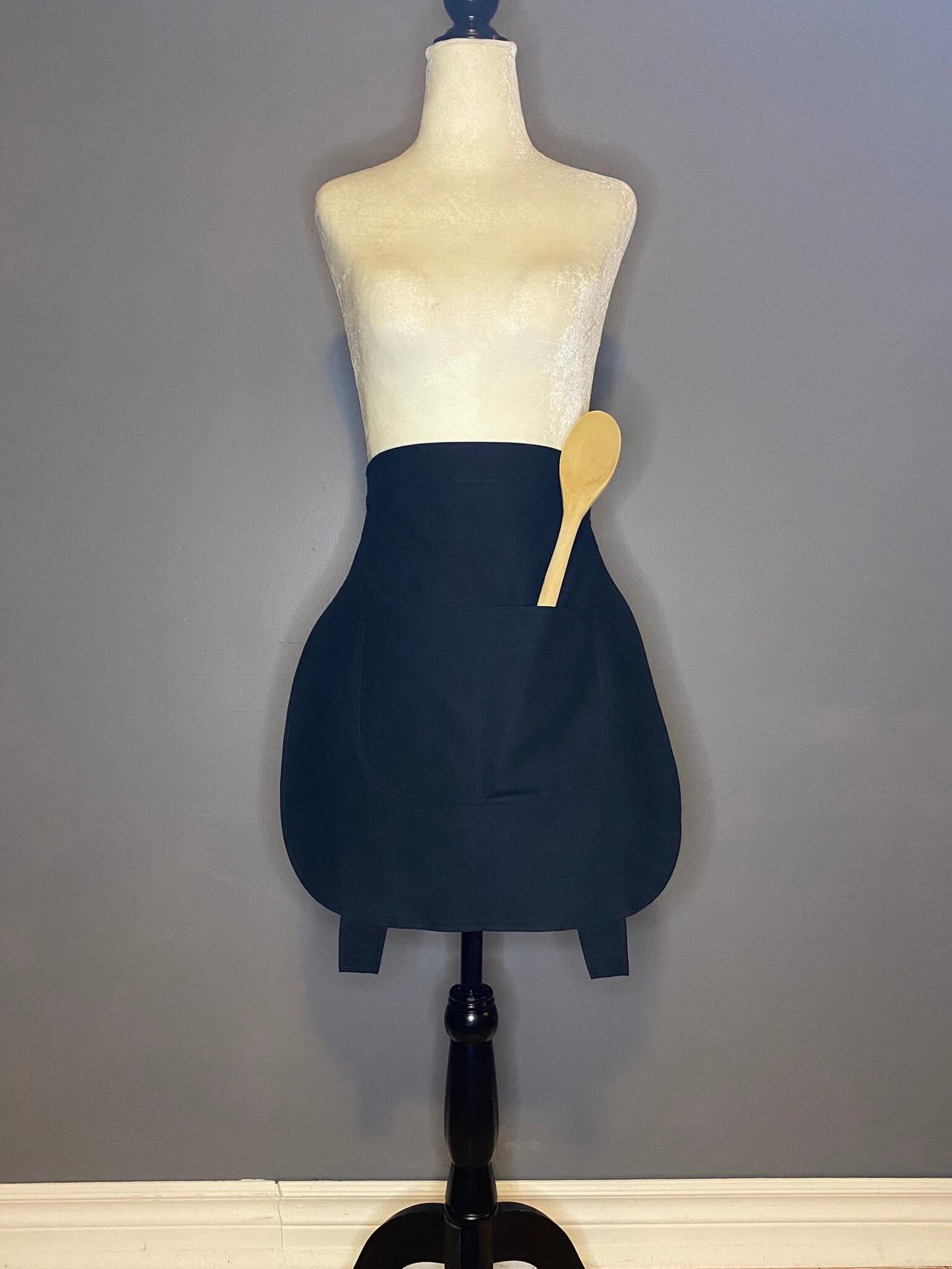 A black, lined cotton linen apron shaped like a cauldron. Featuring little feet, front pockets and a tie for the waist or hips.