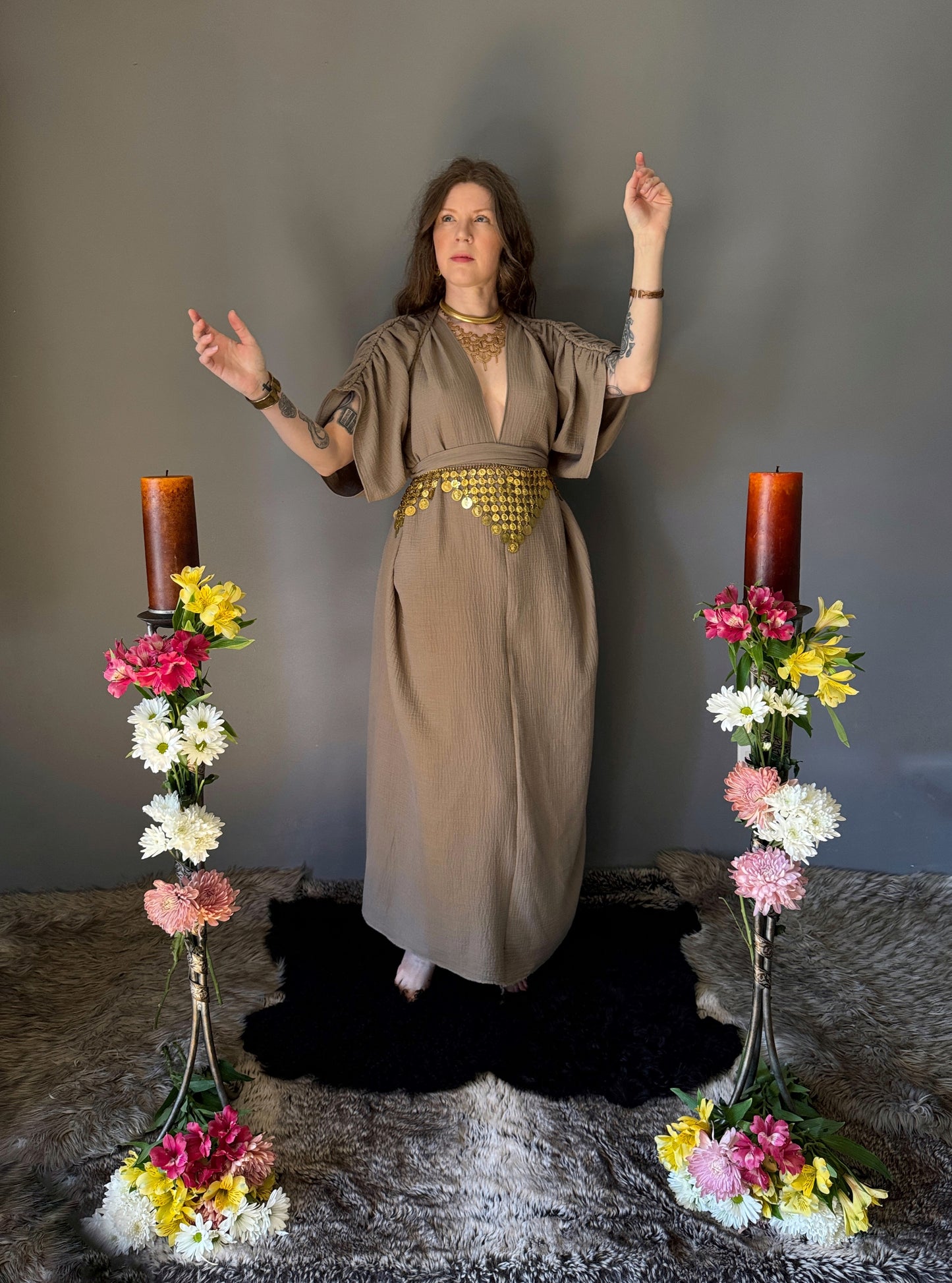 A priestess surrounded by flowers wearing a ancient greek inspired ritual robe. Featuring a deep v neck line, gathered short sleeves with braided trim that ties at the back. Cinched at the waist with a matching long wrap belt. The gown is a soft tan colour cotton with a slight waffle comb texture. The veil is made from a cotton gauze in a natural undyed state. For the magically inclined, witches, priestess, priest, pagan, hellenistic, polytheistic, spiritual or lover of history. Sustainably made in Canada