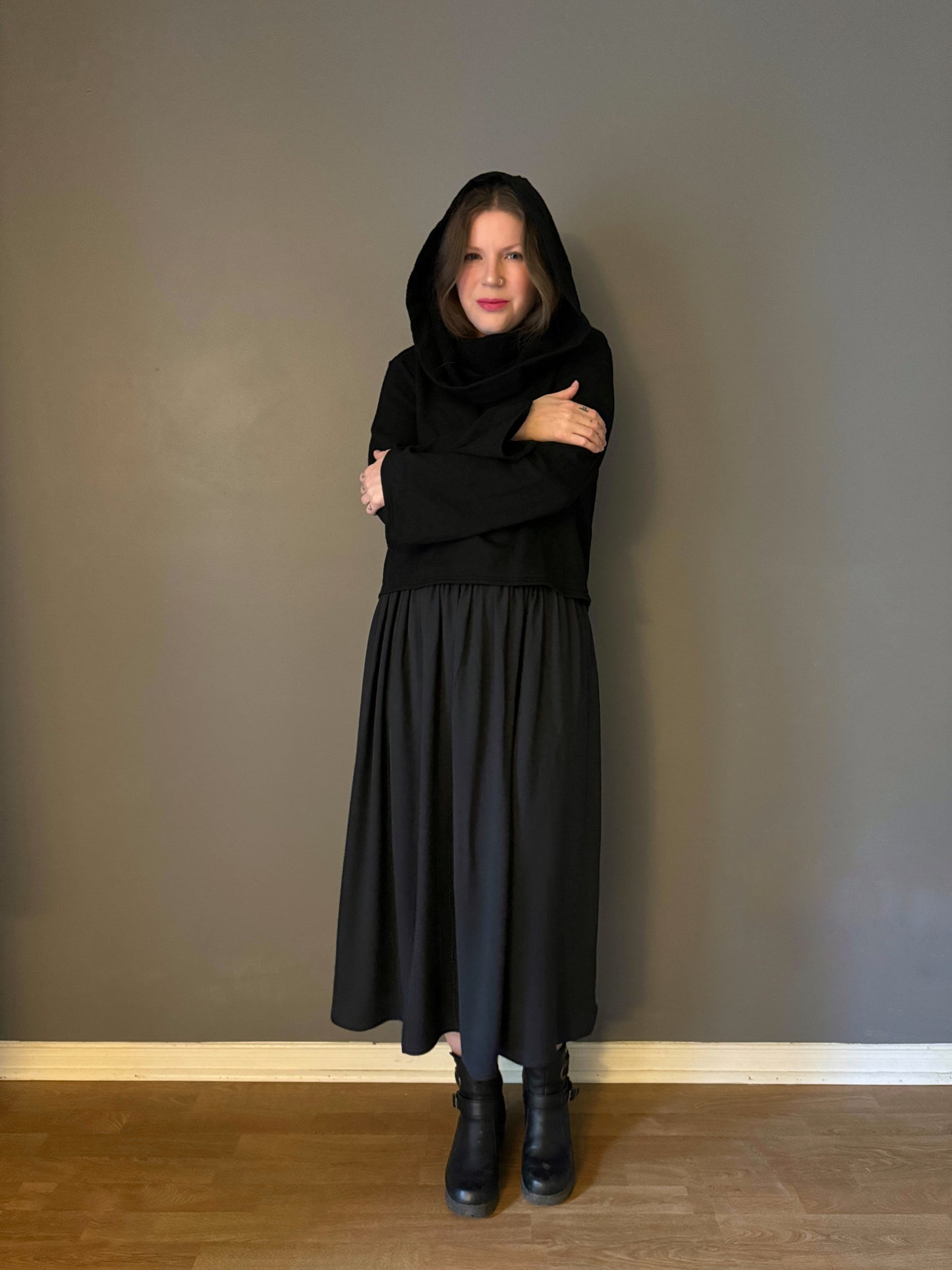 A witch embracing herself in a warm hexen hoodie and black skirt. The hoodie features a large cowl hood and cropped just at top of the hips. Featuring slight bell sleeves and its made from a soft bamboo knit with a fleece interior. Very soft and warm good for layering. Witch clothing, fall wear, sustainably made in canada