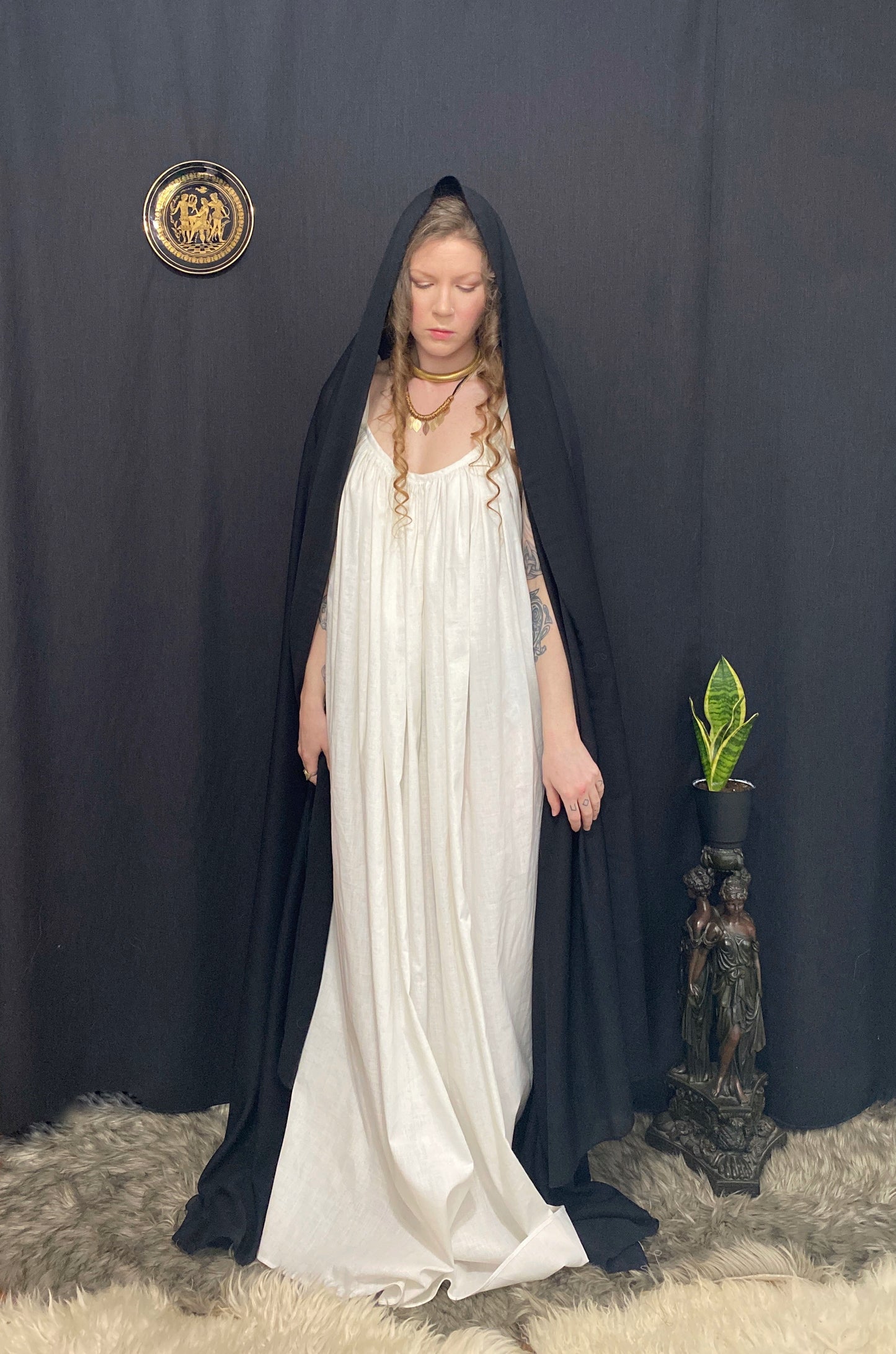 An ancient priestess draped in a white gown and a long black sheer veil over her head. The gown features adjustable straps that tie at the shoulder, side seam pockets and a long belt to bring in the waist. Priestess, ritual wear, sustainable clothing, made in canada