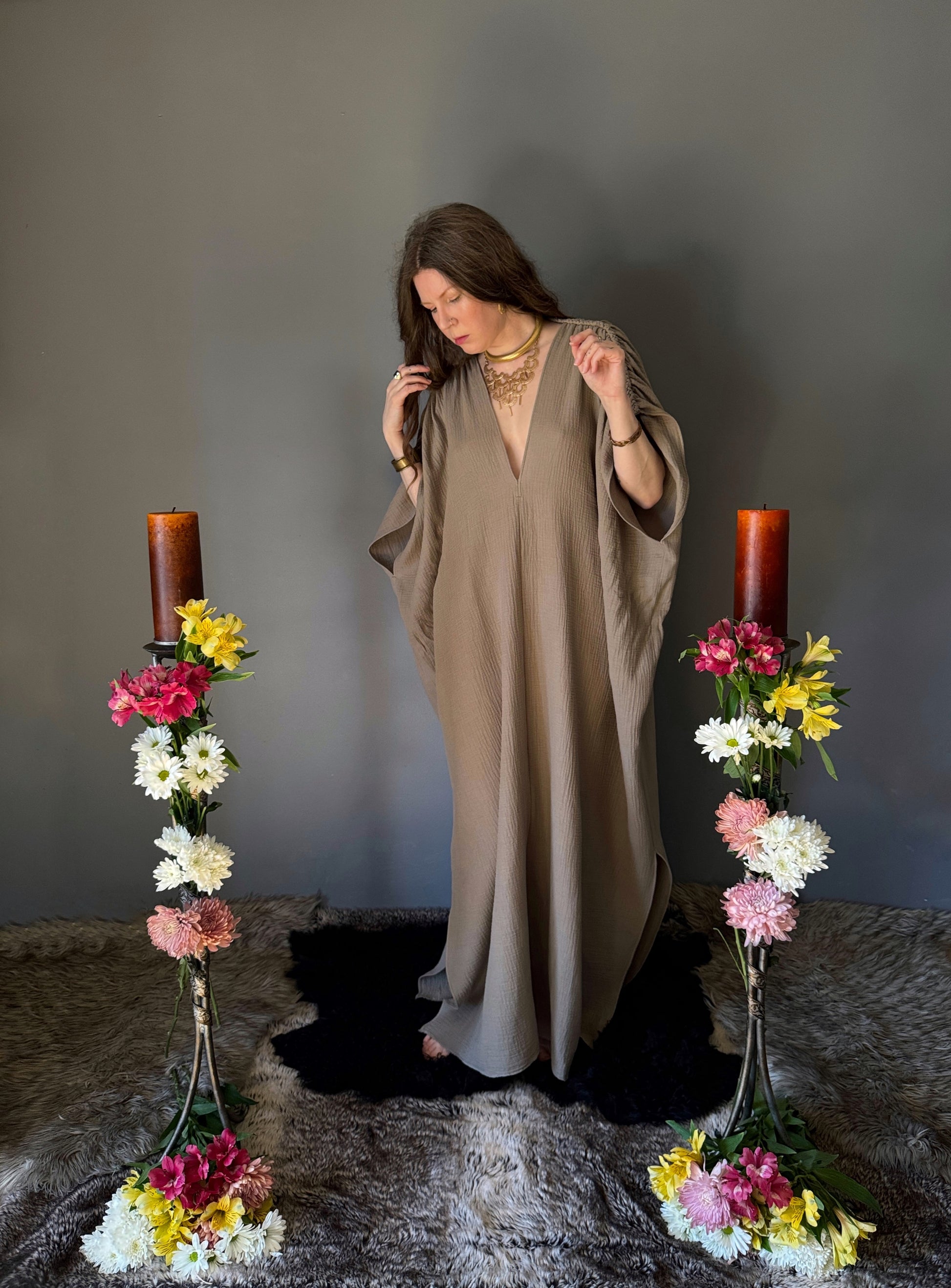 A priestess surrounded by flowers wearing a ancient greek inspired ritual robe. Featuring a deep v neck line, gathered short sleeves with braided trim that ties at the back.  Worn loose in this photo to showcase size variation with a dress circumference of 80". The gown is a soft tan colour cotton with a slight waffle comb texture. For the magically inclined, witches, priestess, priest, pagan, hellenistic, polytheistic, spiritual or lover of history.