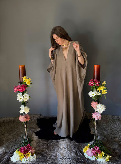 A priestess surrounded by flowers wearing a ancient greek inspired ritual robe. Featuring a deep v neck line, gathered short sleeves with braided trim that ties at the back.  Worn loose in this photo to showcase size variation with a dress circumference of 80". The gown is a soft tan colour cotton with a slight waffle comb texture. For the magically inclined, witches, priestess, priest, pagan, hellenistic, polytheistic, spiritual or lover of history.