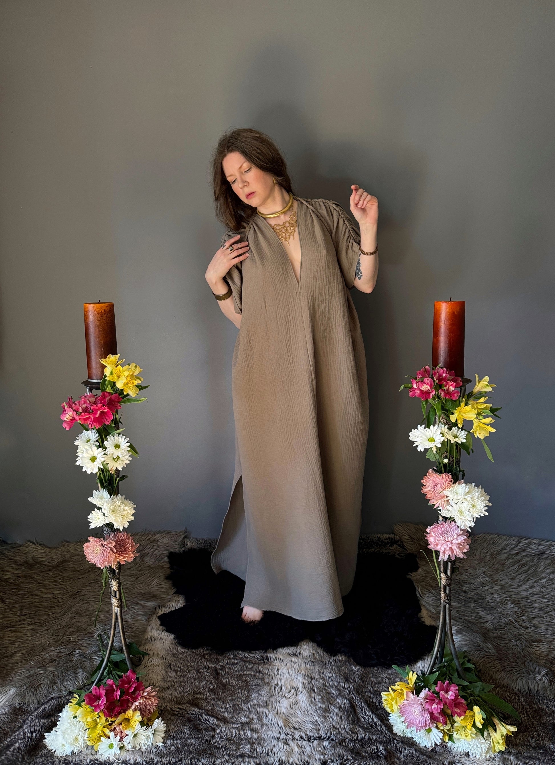 A priestess surrounded by flowers wearing a ancient greek inspired ritual robe. Featuring a deep v neck line, gathered short sleeves with braided trim that ties at the back.  The gown is a soft tan colour cotton with a slight waffle comb texture. For the magically inclined, witches, priestess, priest, pagan, hellenistic, polytheistic, spiritual or lover of history.