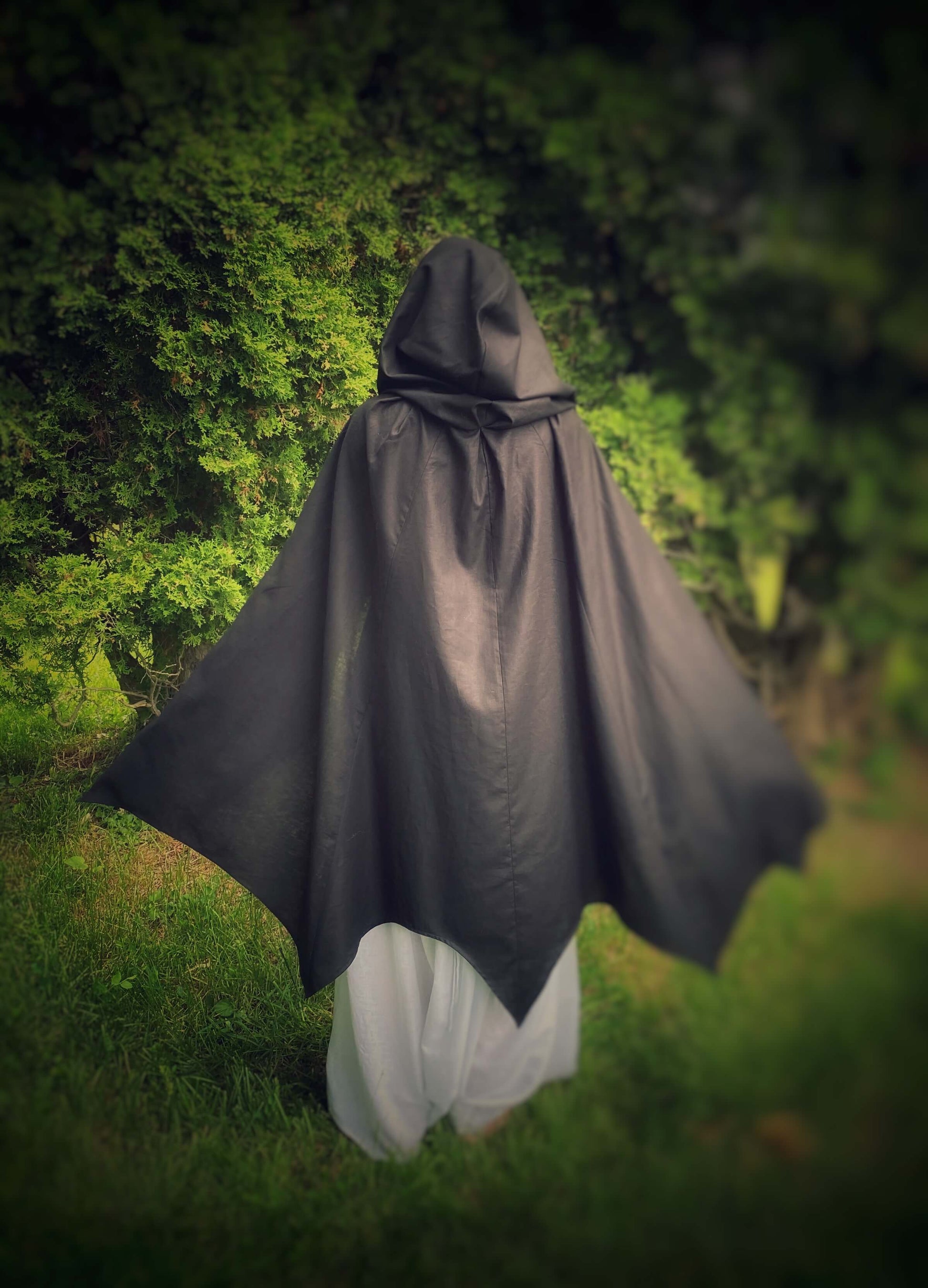 A black, lightweight cape shaped like bat wings. This photo is the back of the cape with the hood up, featuring the bat wing hem.