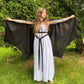 A black, lightweight bat wing shaped cape. The model is holding the cape open by the finger loops to expose the bat wing hem. 