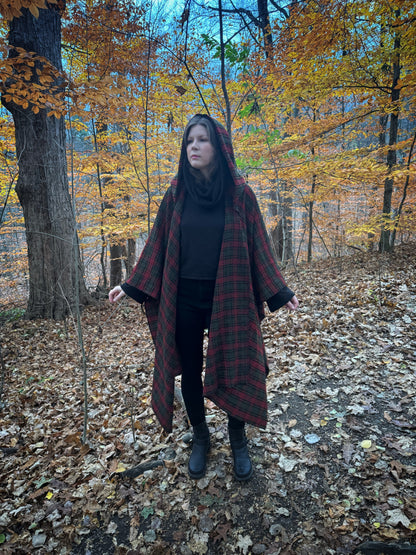 A witch standing in a fprest covered in fallen leaves wearing black pants and a black hexen hoodie with a tartan poncho layered over top. The hoodie features a large cowl hood and cropped just at top of the hips. Featuring slight bell sleeves and its made from a soft bamboo knit with a fleece interior. Very soft and warm good for layering. Witch clothing, fall wear, sustainably made in canada