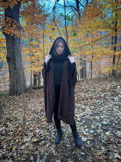 A witch standing in a fprest covered in fallen leaves wearing black pants and a black hexen hoodie with a tartan poncho layered over top. The hoodie features a large cowl hood and cropped just at top of the hips. Featuring slight bell sleeves and its made from a soft bamboo knit with a fleece interior. Very soft and warm good for layering. Witch clothing, fall wear, sustainably made in canada