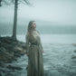 Model is wearing our long sleeve, tunic dress in a natural colour. Standing on a rock, holding a sword with a lake in the background.